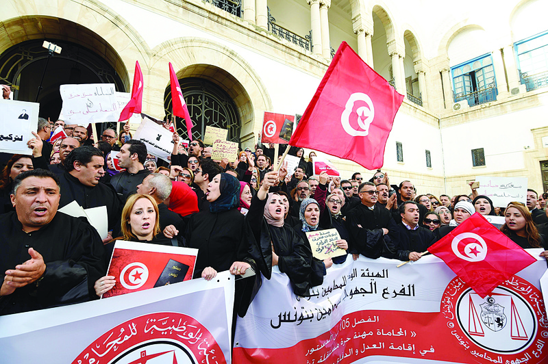 (FILES) In this file photo taken on December 6, 2016, Tunisian lawyers with national flags shout anti-government slogans during a demonstration against a draft 2017 budget that would impose a public sector pay freeze, outside the Tunis law court. - Tunisians may have overthrown dictator Zine El Abidine Ben Ali a decade ago, but with few reforms to the country's security forces and an economy rife with nepotism, its revolution is far from achieving its goals. (Photo by FETHI BELAID / AFP)