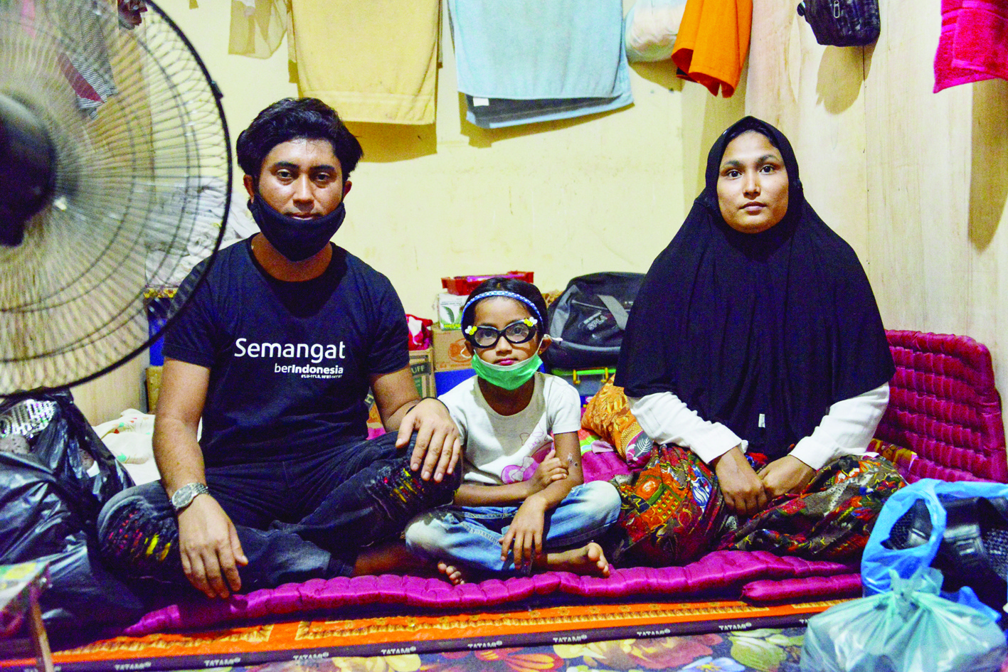 This photo taken on October 22, 2020 shows Rohingya migrant Nemah Shah (L) with his six-year-old daughter Nosmin Fatimah and his wife Majuma (R) after being reunited at a temporary shelter in Lhokseumawe in Aceh province. - Weeks after a funeral for the wife and daughter he thought had died at sea while trying to sail to him, Nemah Shah was stunned when he saw online images of them emerging from a refugee boat in Indonesia. (Photo by CHAIDEER MAHYUDDIN / AFP) / To go with Rohingya-migration-trafficking-family,FOCUS by Haeril Halim