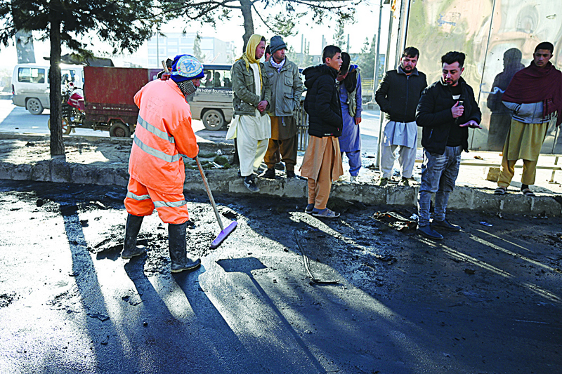 Onlookers watch a municipal workers clean and remove debris along a street after multiple rockets were fired in the Afghan capital Kabul on December 12, 2020. - A series of rockets struck the Afghan capital on December 12, killing one person and wounding another, the interior ministry said, the second such attack to rock Kabul in less than a month. (Photo by WAKIL KOHSAR / AFP)