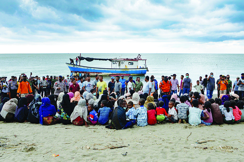(FILES) In this file photo taken on June 25, 2020 Rohingya migrants sit by the beach after their boat landed on the shores of Lancok village, in Indonesia's North Aceh Regency. - Boatloads of Rohingya landing across Southeast Asia are victims of complex human trafficking networks run by a dizzying web of players, from crime bosses and corrupt cops to poor fishermen, rickshaw drivers and even Rohingya themselves. (Photo by CHAIDEER MAHYUDDIN / AFP) / To go with Rohingya-migration-trafficking,INVESTIGATION by Sam Jahan with Haeril Halim in Lhokseumawe, Indonesia and Peter Brieger in Jakarta.