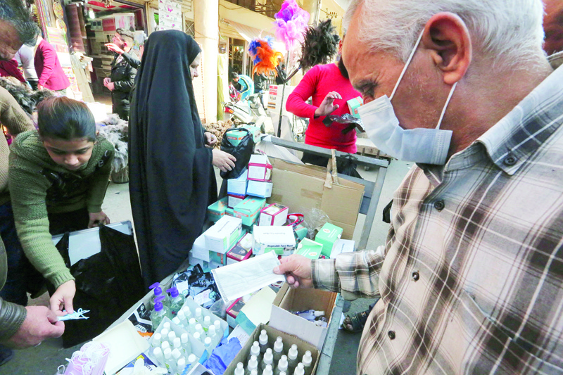 An Iraqi street vendor selling facemasks and disinfectants tends to customers in the capital Baghdad on December 4, 2020. - While much of the world fears Covid-19, Iraqis have mostly stopped wearing facemasks as they worry more about the pandemic's economic impact than the virus itself. In a war-scarred country burdened by rising job losses and deepening poverty, a majority of citizens seem to have shrugged off the global public health crisis. (Photo by Sabah ARAR / AFP)