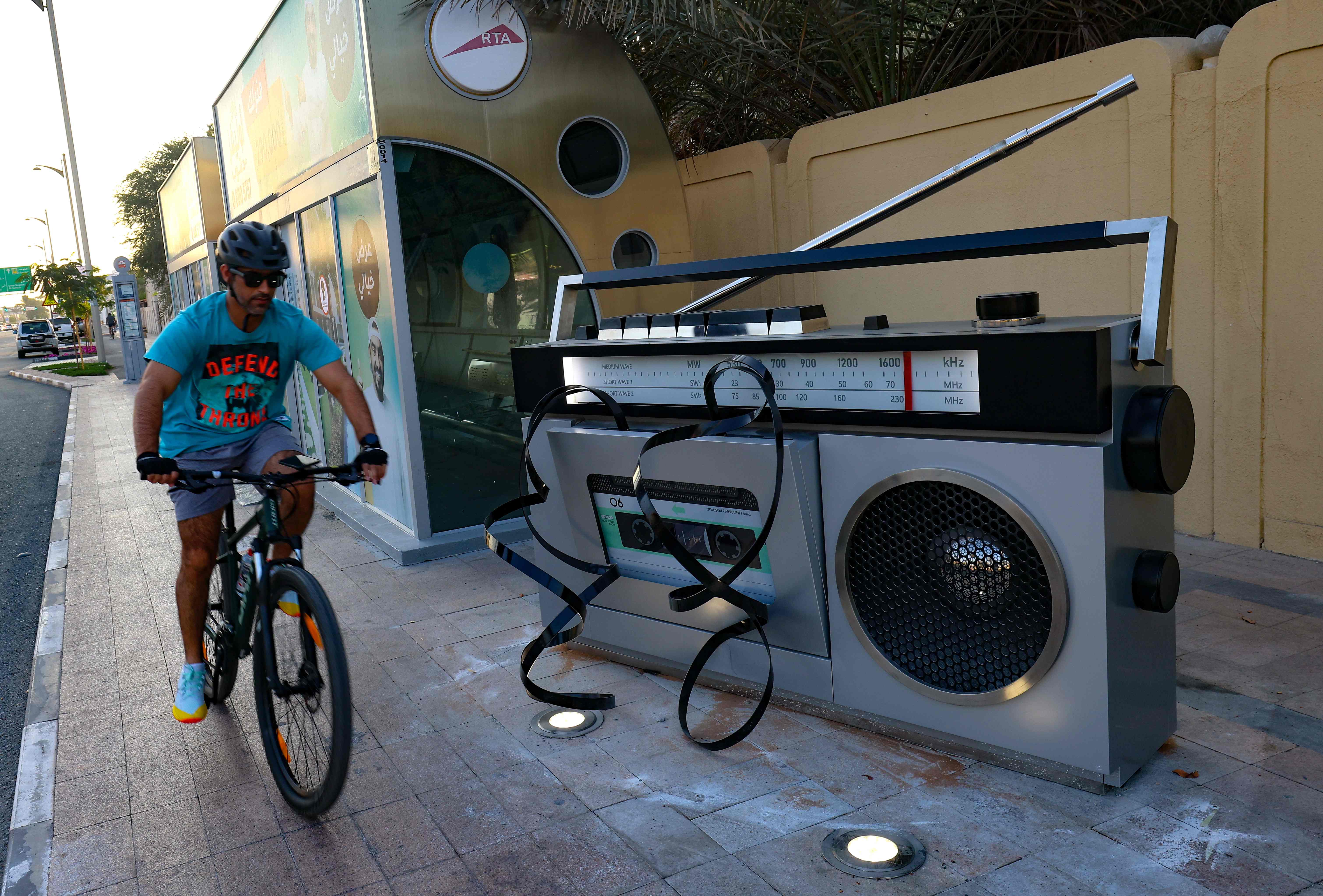 A man rides his bycycle past a giant sculpture representing an old radio-casette recorder on Jumaira street in the Gulf city of Dubai, on December 24, 2020. - The Emirate of Dubai has granted to Jumeirah street, one of its oldest and most popular, a new identity in an attempt to shed light on this vital street that testifies to the rapid development of the desert city. (Photo by GIUSEPPE CACACE / AFP)