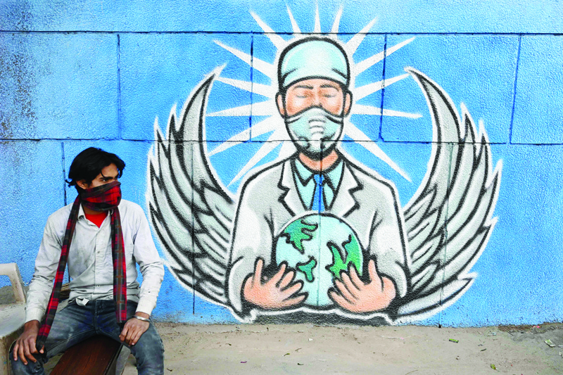A man sits in front of a mural representing a frontline warrior of the Covid-19 coronavirus, painted on a wall along the roadside in New Delhi on December 27, 2020. (Photo by Sajjad HUSSAIN / AFP)