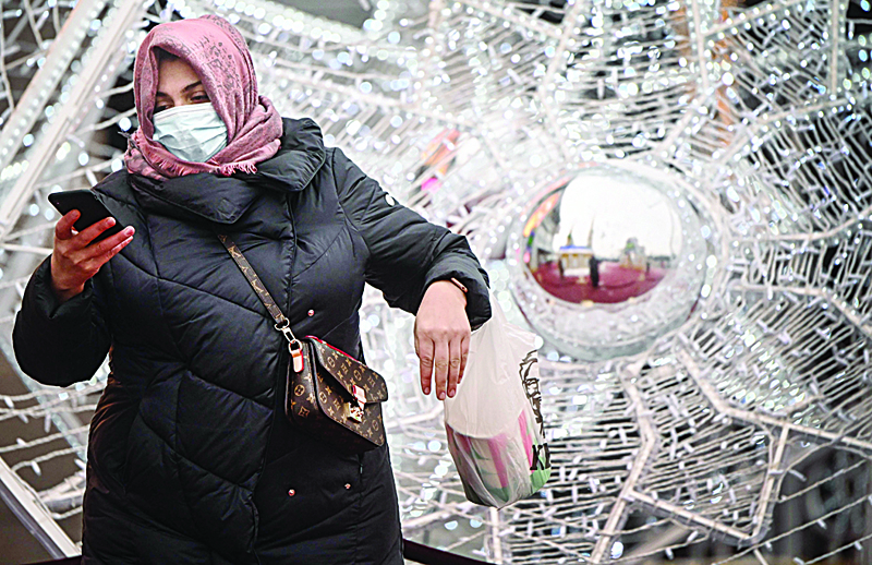 A pedestrian wearing a face mask looks at a smartphone as she walks beside Christmas decorations in front of a shopping mall in Moscow on December 29, 2020, amidst the Covid-19 pandemic caused by the novel coronavirus. - Russia confirmed 27,002 new daily Covid-19 cases including 5,641 in Moscow and 3,757 in Saint Petersburg. (Photo by Alexander NEMENOV / AFP)