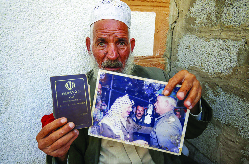 Iranian Qassem Sheyasi holds his Iranian passport and a photo of himself with longtime Palestinian leader Yasser Arafat in his house in Khan Yunis in the southern Gaza Strip, on  November 11, 2020. - His Farsi given name is Qassem Sheyasi but he goes by his Arabic nom-de-guerre Abu Hashem: he used to be longtime Palestinian leader Yasser Arafat's bodyguard and he made quite clear that he is no longer in Gaza by choice. He said he left the Iranian capital 40 years ago to join Arafat's Palestine Liberation Organisation, then based in Beirut, which was one of several armed actors in Lebanon's civil war. (Photo by SAID KHATIB / AFP)