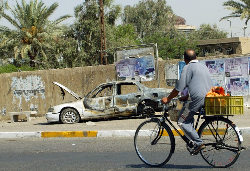 (FILES) In this file photo taken on September 20, 2007 an Iraqi man rides a bicycle passing by a remains of a car, burnt after Blackwater guards escorting US embassy officials opened fire in the Baghdad neighbourhood, on September 16, 2007, killing more than ten people. - Iraqis on December 23, 2020 were outraged, heartbroken but not surprised to hear of a US presidential pardon for four American security guards convicted of killing Iraqi civilians in Baghdad in 2007. The Blackwater team, contracted to provide security for US diplomats in Iraq following the American-led invasion in 2003, claimed they were responding to insurgent fire. The bloody episode left at least 14 Iraqi civilians dead and 17 wounded. (Photo by Ali YOUSSEF / AFP)