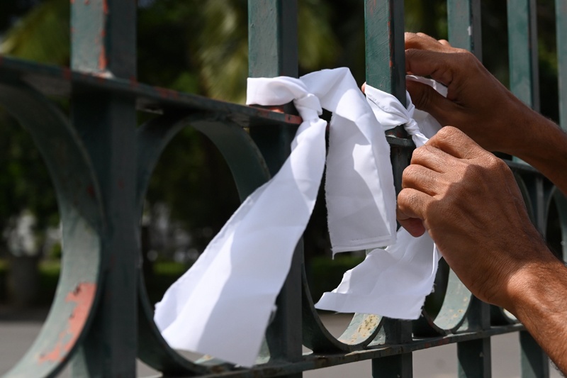 A man ties a white ribbon on a fence at a cemetery as a sign of protest against the government policy of forced cremations of Muslims who die of the coronavirus, in Colombo December 14, 2020. - Sri Lanka said on December 9 it would cremate the bodies of 19 Muslim coronavirus victims, overriding the families' objections against the contentious policy. (Photo by LAKRUWAN WANNIARACHCHI / AFP)