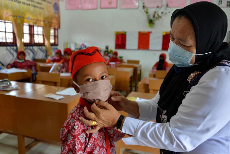 A teacher puts a face mask on a student as a preventive measure against the COVID-19 coronavirus at an elementary school in Banda Aceh on December 2, 2020. (Photo by CHAIDEER MAHYUDDIN / AFP)
