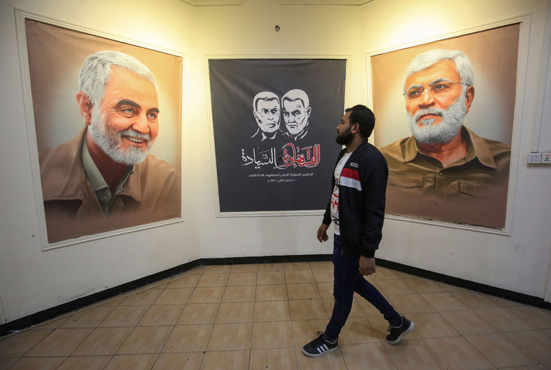 An Iraqi supporter of the Hashed al Shaabi (Popular Mobilisation) paramilitary units walks past posters depicting late Iraqi commander Abu Mahdi al-Muhandis (R) and Iranian Revolutionary Guards commander Qasem Soleimani, at a conference hall in Iraq's capital Baghdad, on December 30, 2020, amid preparations for a ceremony marking the first anniversary of their killing. - On January 3, Iraq will mark a year since a US drone strike killed al-Muhandis, the deputy head of Iraq's powerful Tehran-aligned Hashed Al-Shaabi paramilitary network, alongside Soleimani, head of the elite external operations of Iran's Revolutionary Guards, nearly sparking a conflict that many fear could still ignite. (Photo by AHMAD AL-RUBAYE / AFP)