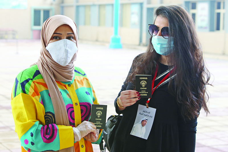 Kuwaiti women, wearing protective masks amid the COVID-19 pandemic, display their passports as they wait to cast their votes at a polling station in Kuwait City during parliamentary elections on December 5, 2020. - Kuwait's parliamentary elections have started under the shadow of Covid-19, with facilities laid on for citizens infected with the disease to vote in special polling stations. The oil-rich country has enforced some of the strictest regulations in the Gulf to combat the spread of the coronavirus, imposing a months-long nationwide lockdown earlier this year. (Photo by Yasser Al-Zayyat / AFP)