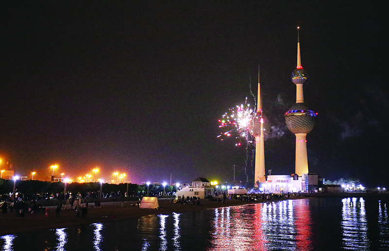 People sitting on the beach as fireworks explode over the Kuwait towers in Kuwait City during the new year's celebrations on January 1, 2021.