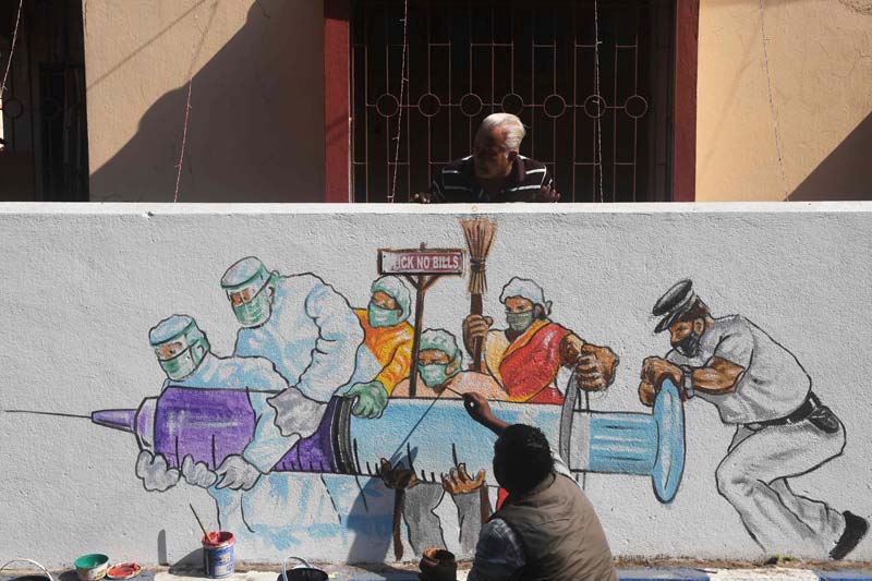 TOPSHOT - Residents look as an artists gives finishing touches to a mural depicting frontline workers carrying a Covid-19 coronavirus vaccine in Kolkata on January 2, 2021. (Photo by Dibyangshu SARKAR / AFP)