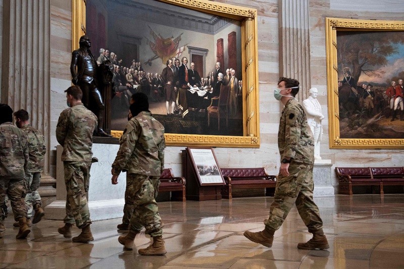 WASHINGTON: Army National Guard members walk past a painting of the Declaration of Independence being ratified while guarding Capitol Hill yesterday. - AFP  n