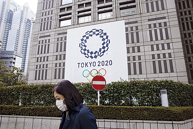 TOKYO: A pedestrian walks past a traffic sign next to an official Tokyo 2020 Olympic Games banner hanging on the Tokyo Metropolitan Government Building on January 22, 2021. - AFPn