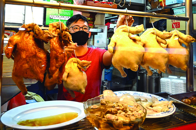 This photograph shows hawker apprentice Lim Wei Keat displaying chickens at a chicken rice stall in Singapore. - AFP photos