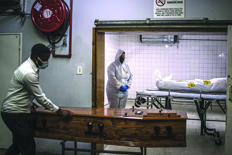 PRETORIA: A morgue attendant at the Pretoria branch of the South African funeral and burial services company Avbob stands still next to the body of a patient died of COVID-19 related illnesses as a coffin being brought along ahead of burial.-AFPn