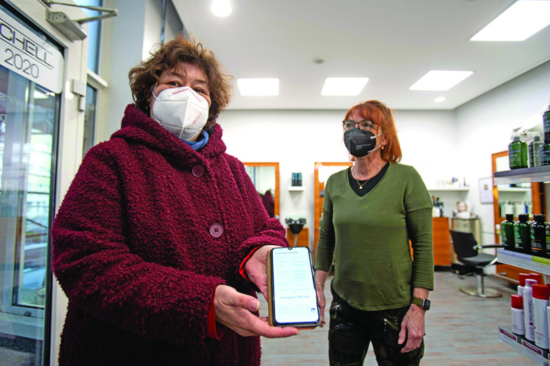 Owner Susanne Schreiber (right) watches as a customer shows her antigen virus test upon entering Schreiber's hairdressing salon in Vienna.-AFP photos n