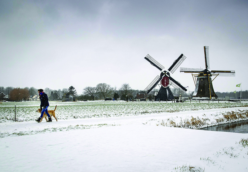UTRECHT, Netherlands: Snow blankets a field as a man and his dog walk past a windmill yesterday. - AFP n