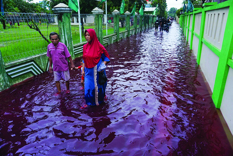 PEKALONGAN, Indonesia: Residents wade through floodwaters dyed red from a batik factory in central Java on Saturday. - AFP n