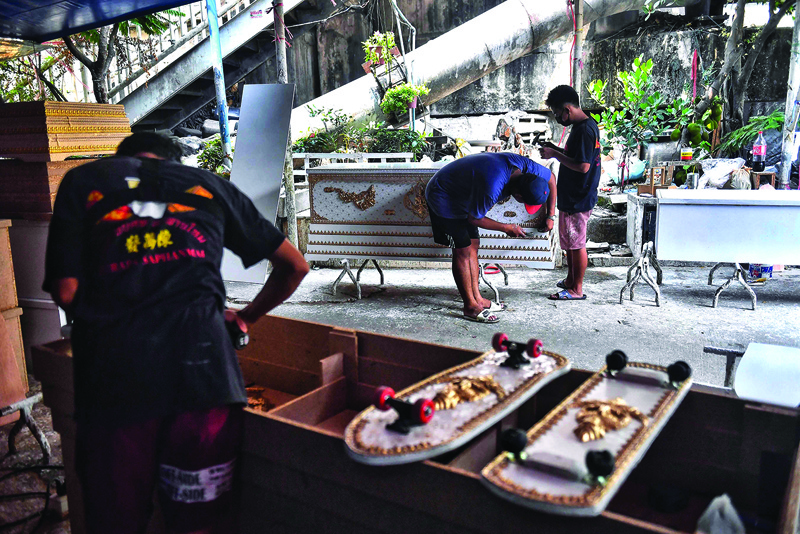 This photo shows employees from the Burapha coffin shop working on a coffin near skateboards, made from wood used for coffins, in Bangkok. -AFP photosn