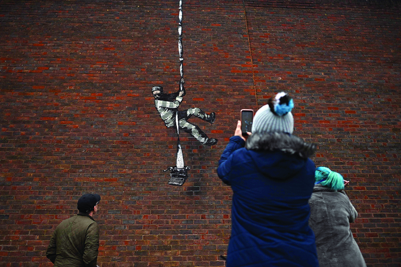 Members of the public pause to take photographs of an artwork bearing the hallmarks of street artist Banksy on the side of Reading Prison in Reading, west of London.-AFP n