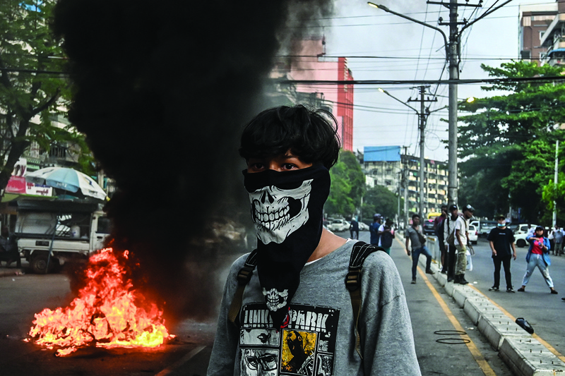 YANGON: A protester with his face covered stands near a burning makeshift barricade along a road during a protest against the military coup, in Yangon on Tuesday.-AFPn