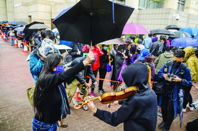 HONG KONG: A supporter plays a violin as others line up outside West Kowloon court in Hong Kong yesterday during court appearances by dozens of dissidents charged with subversion in the largest use yet of Beijing's sweeping new national security law. - AFPn