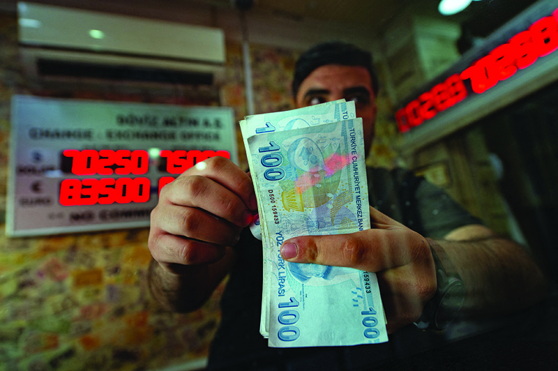 ISTANBUL: A currency exchange office worker counts Turkish Lira banknotes in front of an electronic panel displaying currency exchange rates at an exchange office in Istanbul. – AFPn