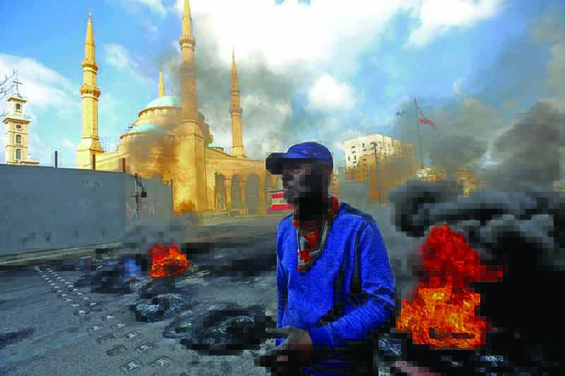 BEIRUT: A man stands next to flaming tires at a make-shift roadblock set-up by anti-government demonstrators next to the Mohammed Al-Amin Mosque in the Martyrs' Square in the center of Lebanon's capital Beirut yesterday during a protest against the deteriorating value of the local currency and dire economic and social conditions. – AFPnn