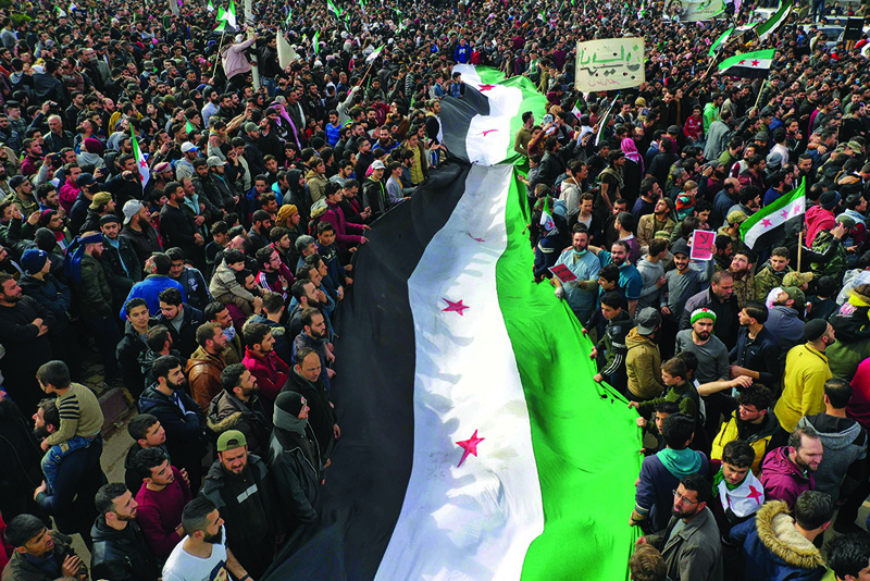 IDLIB: Syrians wave the national flag during a gathering in this rebel-held city yesterday as they mark 10 years since nationwide anti-government protests began. - AFP n