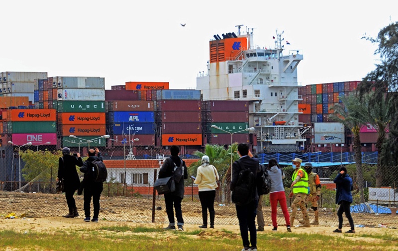 Journalists look at a container ship navigating the Suez Canal yesterday, a day after the Ever Given cargo vessel was dislodged from its banks. – AFP n