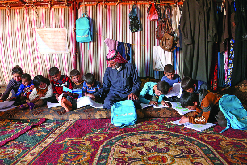 IDLIB, Syria: Abderrazaq Khatoun, helps his 11 orphaned grandchildren with their school work, inside a tent in an encampment in the village of Harbanoush, in the northern countryside of Syria's northwestern province of Idlib.-AFPn