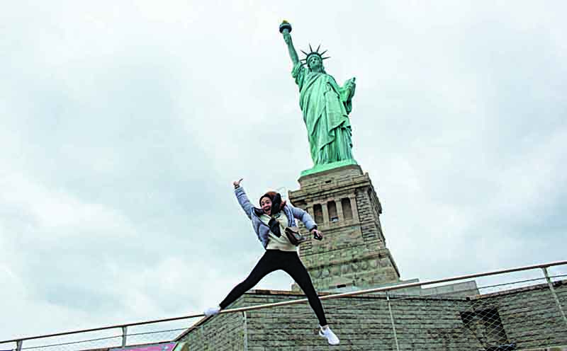 A woman from Michigan jumps as she poses in front of Statue of Liberty in New York City. - AFPn