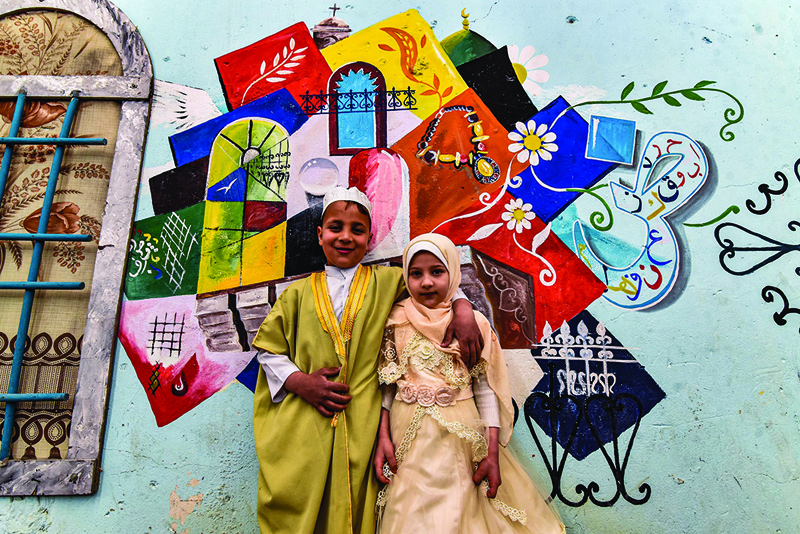 MOSUL, Iraq: Children pose for a photo in front of a large graffiti depicting cultural elements including mosques, churches, old window lattices of the old town of Iraq's northern city of Mosul on the first night of the Muslim holy fasting month of Ramadan yesterday during a celebration hosted by a local cultural NGO. - AFPn