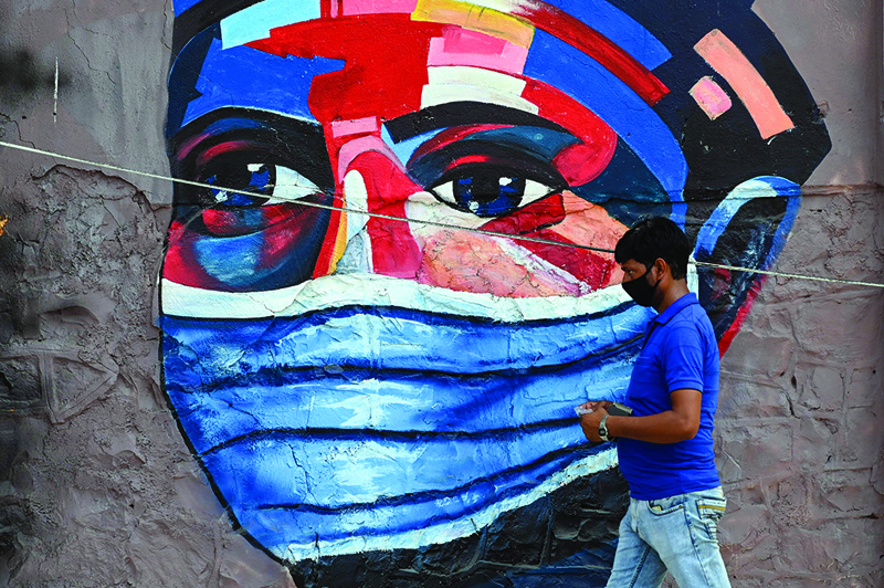 A pedestrian walks past a wall mural depicting a person wearing a protective mask in Mumbai yesterday.-AFP n