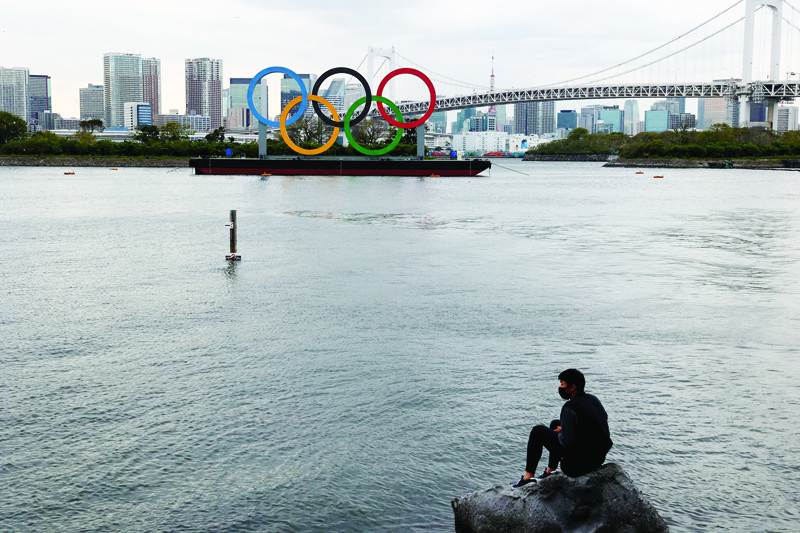 TOKYO: A man sits on a rock in front of the Olympic rings at the Odaiba waterfront in Tokyo on Monday. – AFPn