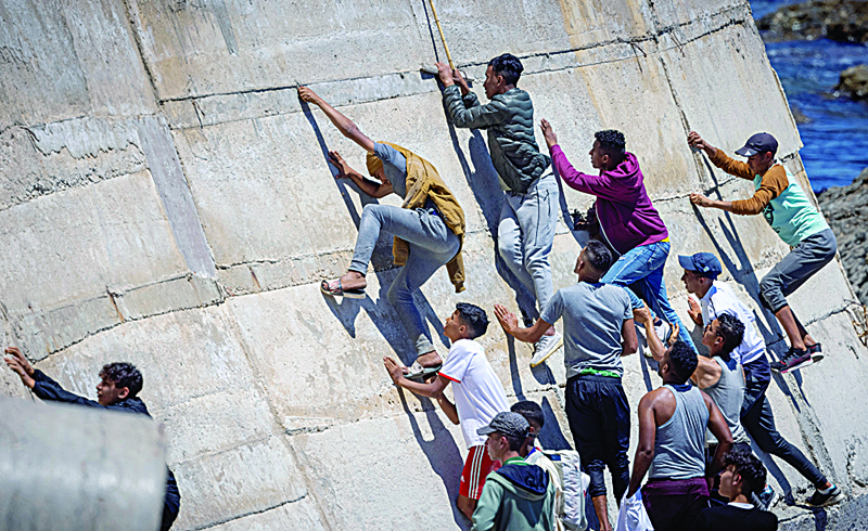 Migrants climb a sea wall in the northern town of Fnideq after attempting to cross the border from Morocco to Spain's North African enclave of Ceuta Wednesday. - AFPn