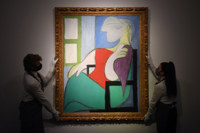 In this photo taken on April 22, 2021, gallery workers display an artwork titled 'Femme assise pres d'une fenetre (Marie-Therese)' by Spanish painter Pablo Picasso during a photocall at Christie's auction house in central London. - AFP nn