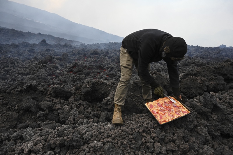 David Garcia places a pizza on a lava river that comes down from the Pacaya volcano at the Cerro Chino hill in San Vicente Pacaya municipality, Guatemala, on May 11, 2021. - AFP photos n