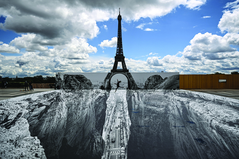 People walk on the esplanade des Droits De L'homme at the Trocadero Square in front of the Eiffel Tower, where a giant artwork by French street artist and photographer Jean Rene, aka JR, is on displayed in Paris.-AFP nn