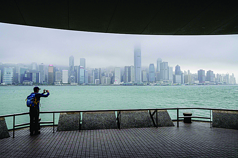 HONG KONG: A man takes photos as he stands on a Kowloon promenade next to Victoria Harbor that provides views of the city skyline yesterday. - AFP n