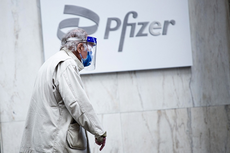 In this file photo a man wearing facemask and shield walks past the Pfizer headquarters in New York on March 11, 2021, one year after the pandemic was officially declared. - Pfizer sharply increased its projections for 2021 revenues and profits on May 4, 2021, citing much higher sales from its Covid-19 vaccine sales.The drugmaker now estimates 2021 revenues of $26 billion from the vaccine, up from $15 billion previously and reflecting 1.6 billion doses expected to be delivered this year under contracts signed through mid-April. - AFP