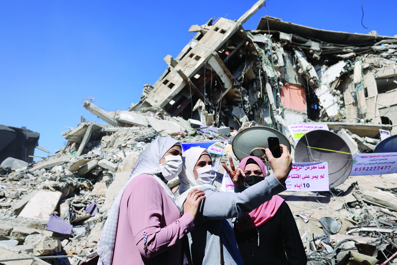 GAZA CITY: Palestinian women pose for a 'selfie' picture in front of a demolished building in the Al-Remal commercial district in Gaza City, recently targeted by Israeli air strikes, yesterday. -AFPnn