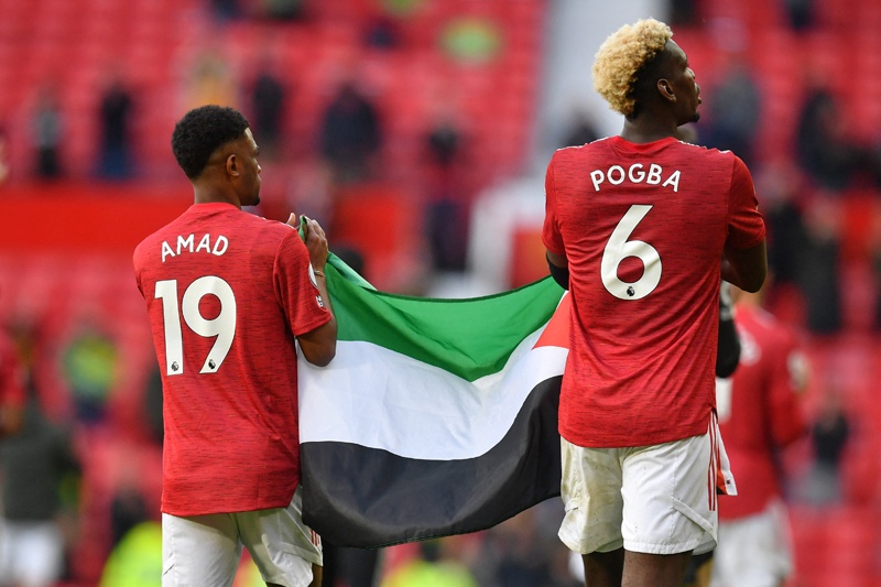 MANCHESTER: Manchester United's French midfielder Paul Pogba (left) and Manchester United's Ivorian midfielder Amad Diallo walk around the pitch while carrying a Palestinian flag at the end of the game during the English Premier League football match between Manchester United and Fulham at Old Trafford in Manchester, north west England, on Tuesday. – AFPnn