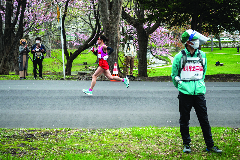 SAPPORO: A volunteer (right) holds a placard asking people to refrain from watching the competition to prevent the spread of the COVID-19 coronavirus while an athlete (center) competes in the half-marathon race which doubles as a test event for the 2020 Tokyo Olympics, in Sapporo on May 5, 2021. - AFPnn