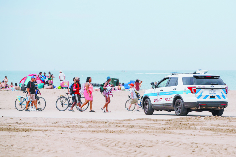 CHICAGO: Beachgoers walk by a Chicago Police officer monitoring the beach from his car in the North Avenue Beach area in Chicago, Illinois, Friday. - AFPn