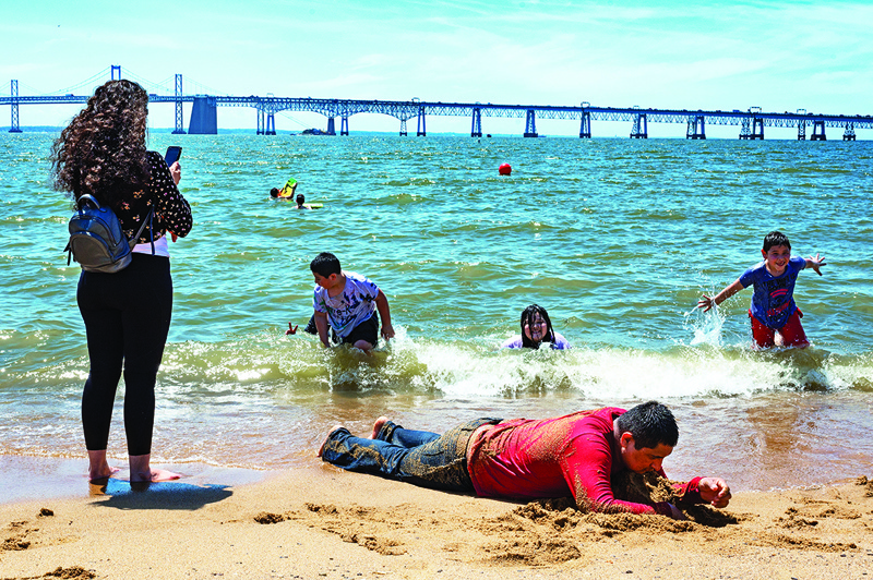 ANNAPOLIS, US: A man lies on the beach as his family plays in the Chesapeake Bay trying to escape the heat at Sandy Point State Park in Annapolis, Maryland Tuesday. - AFPn