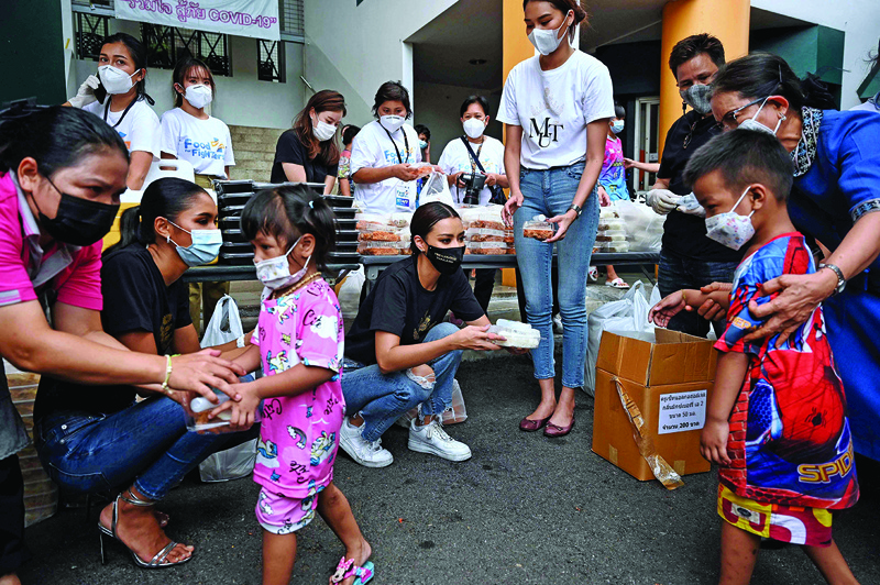 Thai beauty queens Miss Universe Thailand 2020 Amanda Obdam (center), Miss Universe third runner-up Praewwanich Ruangthong (left) and Miss Universe Thailand 2019 contestant Patrapong Wang (centre right) hand out food boxes made by Michelin-starred chefs to children in the Klong Toei slum area of Bangkok yesterday .— AFPn