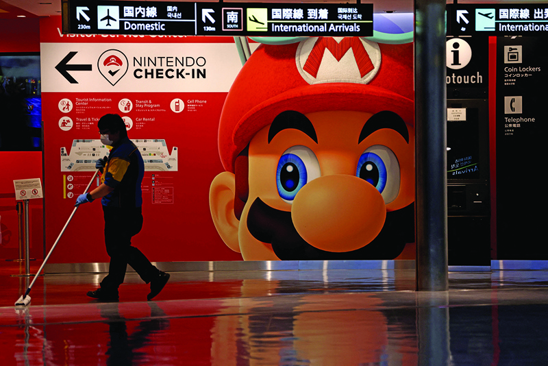 A cleaner mops the floor in front of a Nintendo's Super Mario game character decoration at Narita Airport in China prefecture. - AFP n