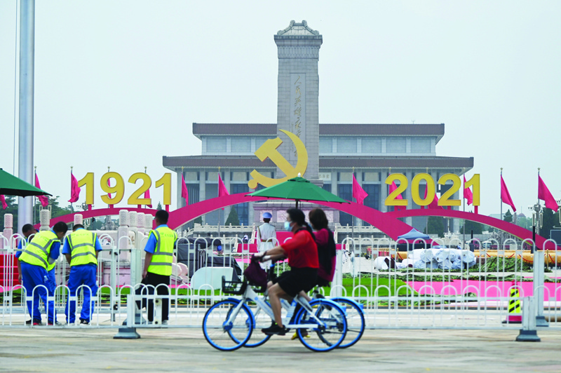 BEIJING: Cyclists ride past as workers adjust a barrier near decorations in Tiananmen Square a day before an event marking the 100th anniversary of the founding of the Communist Party of China, in Beijing yesterday.-AFPn